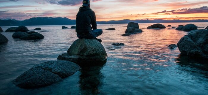 man sitting on rock in ocean at sunrise setting goals